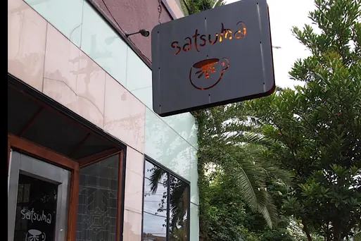 The sign and door of Satsuma Café on Dauphine Street, with sidewalk seating under a tree.