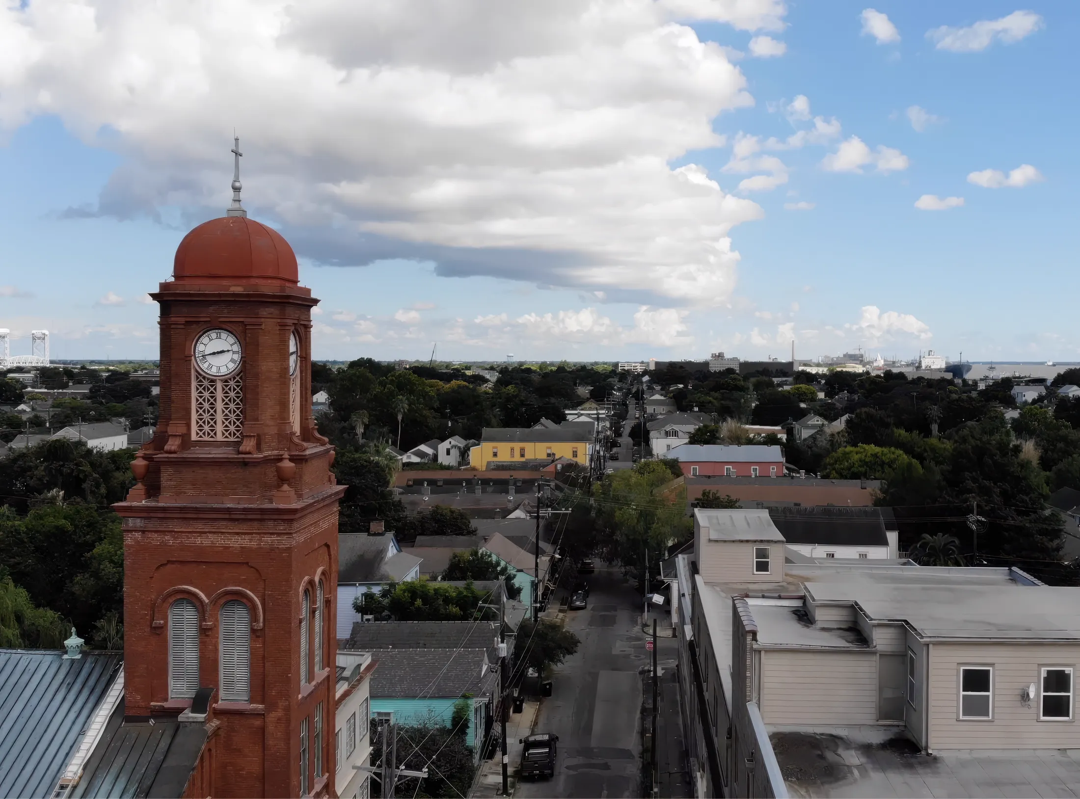 A red-brick clock tower above Bywater rooftops, with the Mississippi River in the distance.