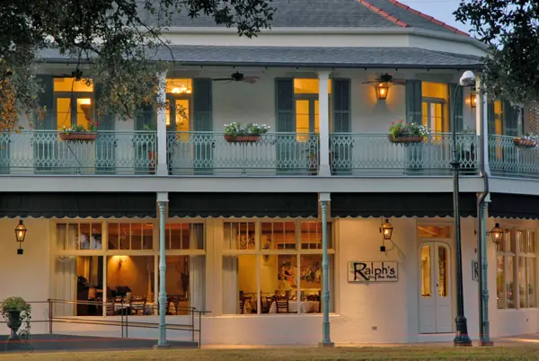 The two-story front of Ralph’s on the Park at dusk, with a teal iron balcony and lit windows.