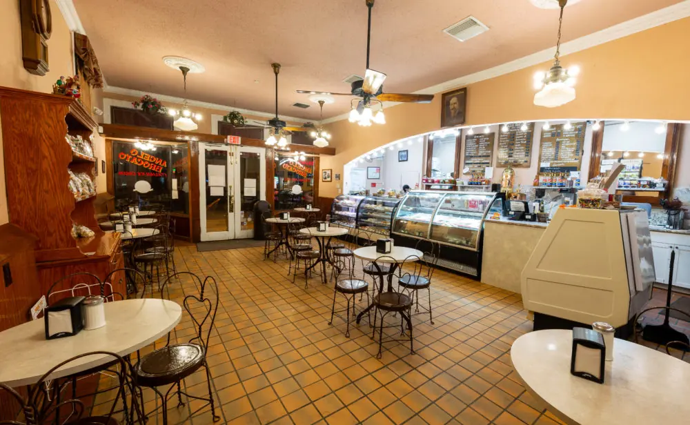 Inside Angelo Brocato, with a tile floor, a long pastry case, ceiling fans and small cafe tables.