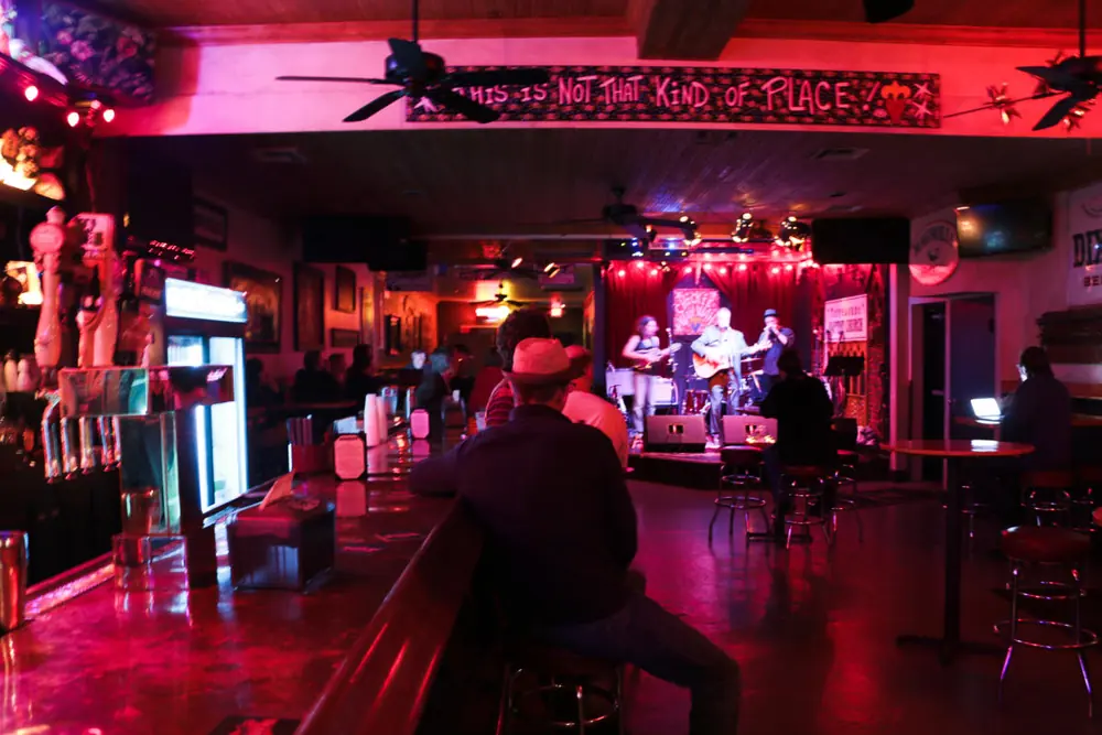 A band on the small stage at Chickie Wah Wah, lit in red and pink, with the bar in the foreground.