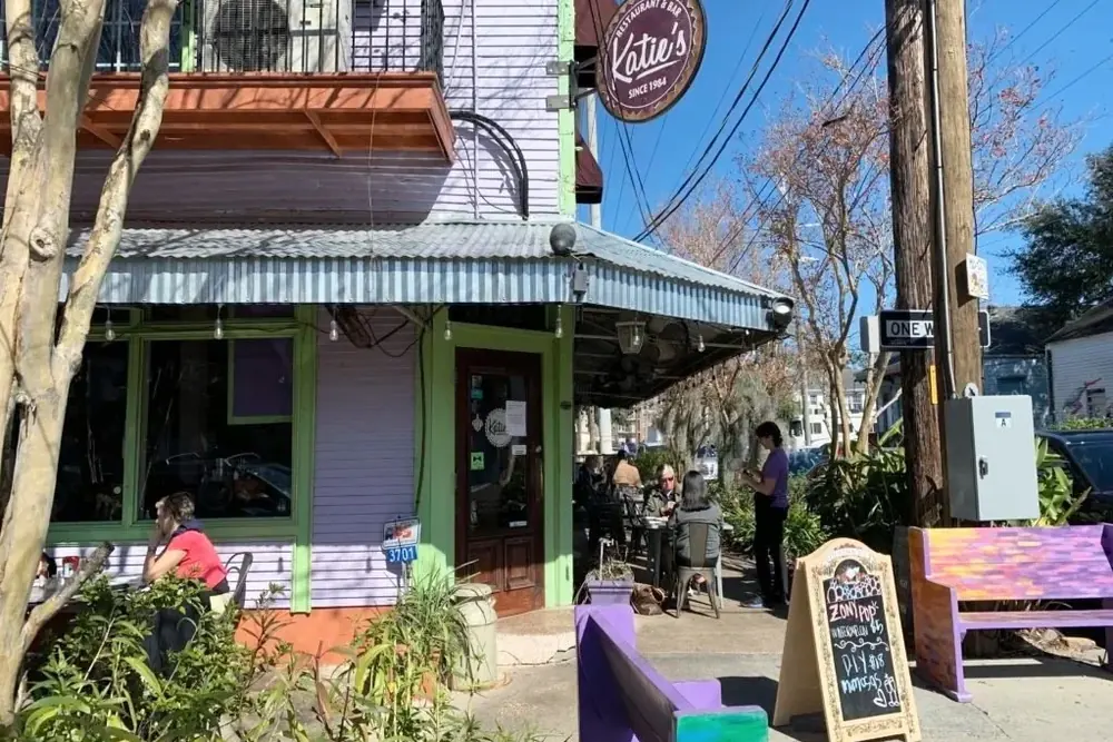 The purple corner building of Katie’s with a green-trimmed door, a corrugated awning and a chalkboard sign out front.
