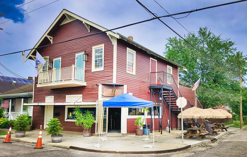 Mid City Yacht Club, a red two-story wooden building with a balcony, outdoor tables and a blue tent.