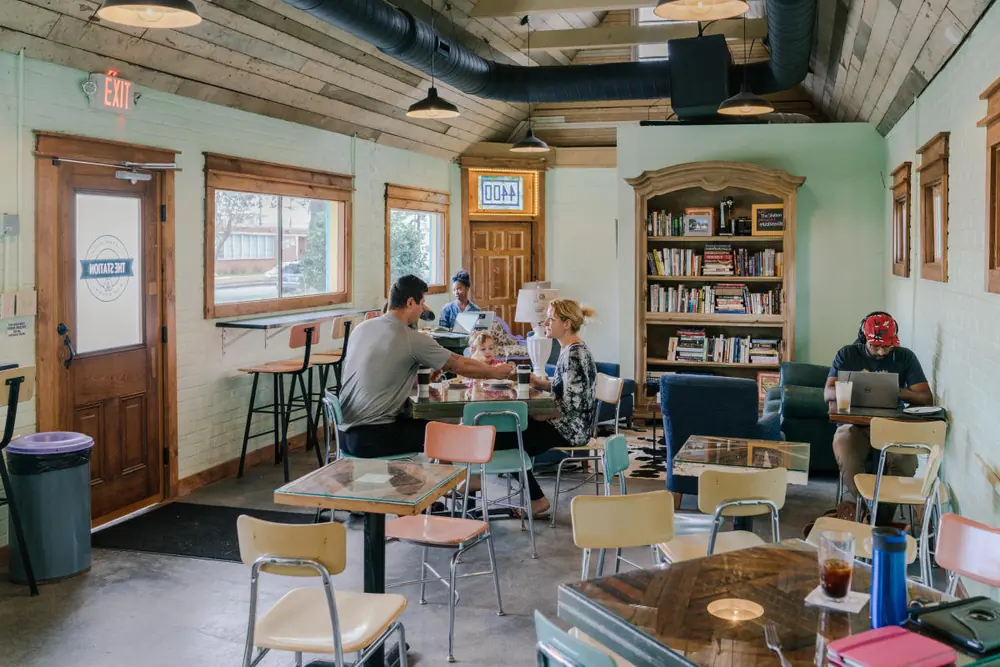 Inside The Station, a small coffee shop with wood-framed windows, a bookshelf, cafe tables and customers.