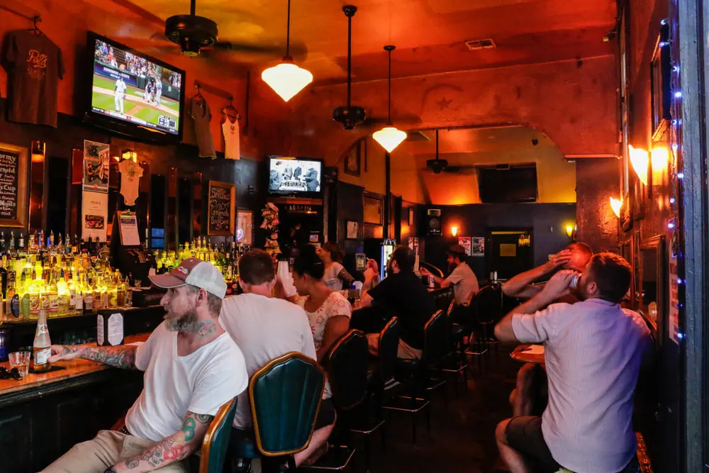 The crowded bar at Pal’s Lounge, lit in amber, with a TV above shelves of liquor.