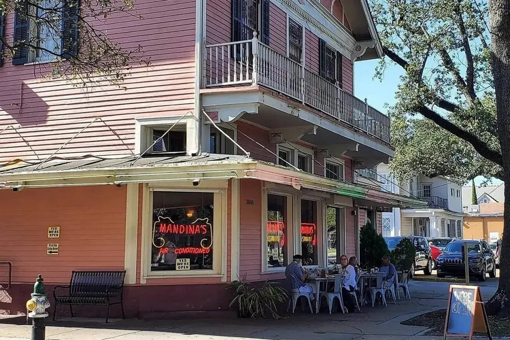 The pink two-story corner building of Mandina’s on Canal Street, with sidewalk tables under oak branches.