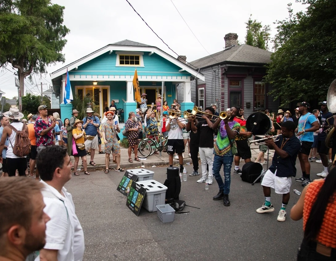 A brass band performs for a crowd outside a turquoise neighborhood house in New Orleans.