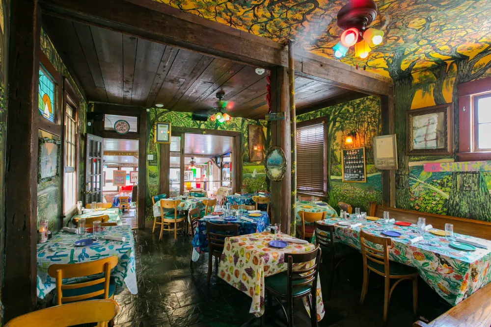The painted, plant-covered dining room at Jacques-Imo’s, with tables in colorful cloths.