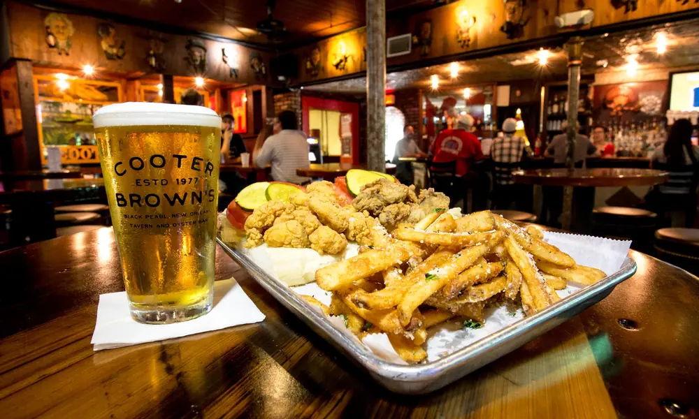 A pint of beer and a tray of fried seafood and fries on a table in the warm, dim bar at Cooter Brown’s.