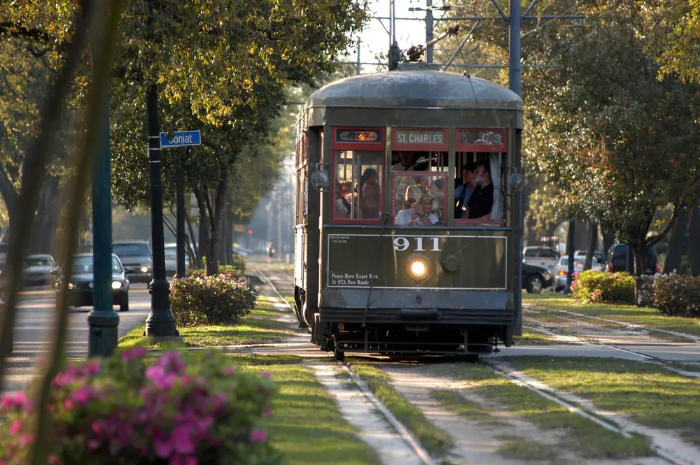 A green St. Charles streetcar, number 911, running down a tree-lined strip of grass.